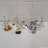 Overview of eleven vintage decorative bells including clear glass and ceramic with colorful and blue/white designs, Disney and Ansley England styles