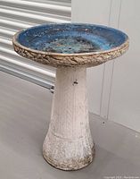 Side view of the birdbath showing the white concrete hollow pedestal with leaf pattern and blue basin with decorative edge.