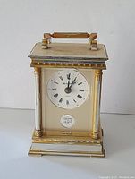Front view of vintage Bulova desk clock showing gold and silver-tone columns and Roman numeral clock face with a small plaque below.