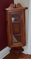 Frontal image of vintage wooden corner shelf with glass door, showing door closed and shelf reflection