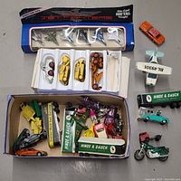 Overview of the entire collection showing jet fighters in packaging, boxes of toy construction vehicles, and loose die cast vehicles including a motorcycle and Hot Wheels car.