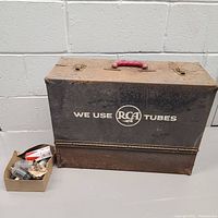 Rusty large metal black RCA branded tube sales box with red handle, closed, with small box of tubes and parts at side.