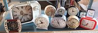 Wide view of twelve vintage and retro style clocks arranged on a table showing varied designs and colors