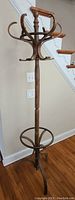 Full view of the entire wooden coat rack showing the tall slender pole, curved top hooks, and circular base support on hardwood floor.