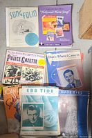 Group photo of vintage sheet music and magazines including colorful covers and a sports magazine.