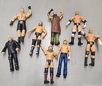 Nine wrestling action figures laid flat on a gray surface, depicting various WWE and WCW wrestlers in different wrestling attire and poses.