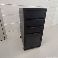 Full view of the black wheeled Ikea Filiny cabinet with three drawers, showing front and wheels.