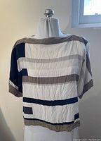 Front view of a women's silk blouse with a geometric pattern in white, taupe, navy, and mustard, displayed on a mannequin.
