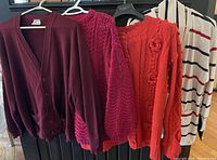 Four cardigans and sweaters on hangers showing full view; burgundy, raspberry pink, red with floral details, white with navy stripes