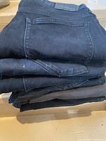Stack of six pairs of black men's jeans folded, back pockets visible, showing signs of wear and vintage condition.