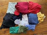 Fabric remnants laid out on wooden floor showing various colors and types including solids of red, yellow, blue, green, white, black, and grey