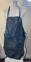 Front view of the large black leather apron displayed on a mannequin, showing full length and front pockets.