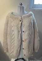 Front of large cream wool knitted sweater with cable details and wooden buttons.