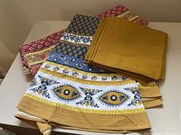 Lot of colorful patterned and solid mustard yellow cotton napkins and two patterned table cloths on a white background.