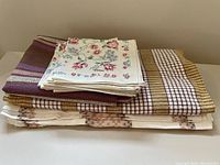 Stack of folded vintage linens showing tablecloth, fabric remnant, and napkins with floral and checked patterns.