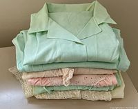 Stacked view of folded sleepwear items showing mint green, cream, and pink fabrics with lace trim