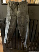 Full view of black leather pants showing front pleats, belt loops, and overall tailored design.