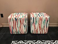 Front view of two cube-shaped swivel ottomans with colorful abstract vertical streak pattern upholstery.