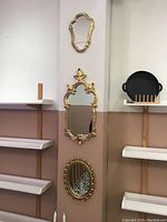 Vertically aligned three gold vintage mirrors on wall: small shield-shaped, large floral-scroll, oval ornate frame