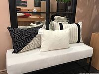 Wide shot of the three throw pillows displayed on white bench with mirror background showing black and white patterned pillows.