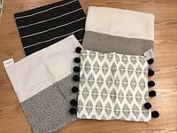 Four decorative throw pillow cases arranged on wooden surface, showing different neutral and black/white patterns and textures.