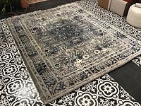 Full view of the 8x10 rug on patterned black and white tile floor showing its overall design and color tones of blue, white, and grey.