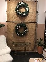 Full view of the 8'x10' jute rug hanging vertically with diamond pattern and two wreaths for scale.