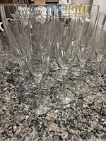 12 clear glass champagne flutes arranged closely together on a speckled countertop.