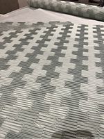 Close-up front view of grey faux fur fabric bolt with raised textured geometric pattern showing width and texture.