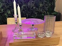 Full view of the vintage crystal and glassware set including candlestick holders with candles, pedestal cake stand, ribbed glass tumblers stacked, rectangular tray, and two small round candle holders on a wooden table.