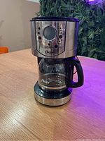 Oster coffee machine front view showing control panel, glass carafe, and stainless steel body.