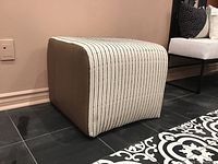 View of the ottoman showing the striped fabric top and brown fabric sides.