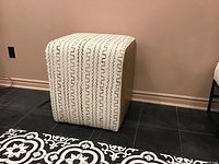 Full view of the ottoman showing the white mud cloth fabric with black geometric designs on top and tan vegan leather sides.