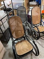 Three black bentwood rocker frames with woven cane seats and backs in storage area