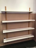 Front view of four white shelves mounted on natural wood vertical supports against a two-tone wall