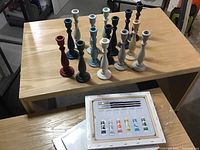 14 chalk painted wooden candlesticks of various colors arranged on a wooden table with visible paint chips.
