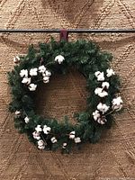 Single artificial pine wreath with cotton bolls hung against a tan textured background for display