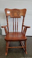 Front view of antique child's rocking chair showing carved backrest and armrests, spindled legs and rockers.