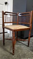 Front-right angle view of antique wooden corner chair showing upholstery and wooden spindle backrest.