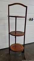 Front view of the antique wooden cake stand showing two circular tiers and curved handle.