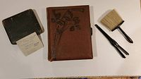 Group photo of antique hat pin tool/glove stretcher, clothing brush, vintage silverplate spoons case and 1941 music box photo album
