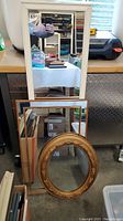 Three mirrors stacked: a 21 inch rectangular white framed mirror, a larger rectangular thin framed mirror, and an oval gold ornate mirror.