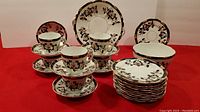 Tea set arranged showing stacked side plates, cups on saucers, cake plate and bowl with Imari-style floral patterns.