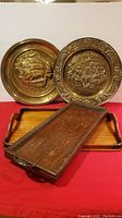 Photo of two large antique brass plates with detailed designs and two wooden trays, one narrow with brass corner brackets and engraving.