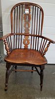 Full front view of antique Windsor back chair with armrests showing carved central splat and turned legs.