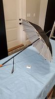 Side angle showing full parasol length and handle resting on table, highlighting its old-fashioned wooden handle and curved tip.