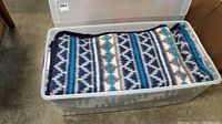 Plastic bin containing folded blue and white geometric pattern blanket