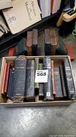 Top view of 8 antique and vintage bibles in a cardboard box showing varying sizes and cover colors.