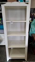 Frontal view of white wooden bookshelf showing three shelves, clean condition with a decorative wavy top.