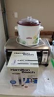 Full lot showing Hamilton Beach cordless kettle in box, Rival crock pot with floral design, and Rival convection oven below